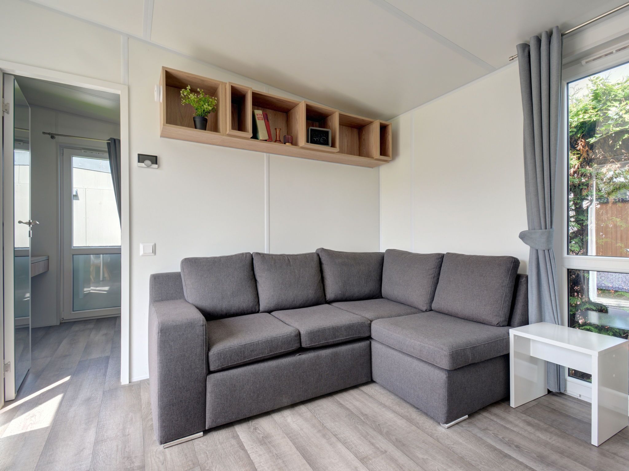 Una sala de estar moderna con un sofá seccional gris, un escritorio blanco y estanterías de madera empotradas sobre el sofá.