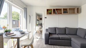 Ein modernes Wohnzimmer mit einer grauen Couch, einem Esstisch mit Stühlen und einer durch eine offene Tür einsehbaren Küchenzeile.