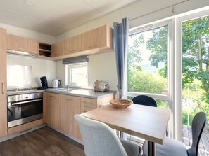 Una cocina moderna con armarios de madera, estufa a gas, un lavabo y un ventanal con vistas al verdor.