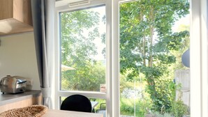 Une cuisine équipée d’un grille-pain, d’un panier en osier et offrant une vue sur un jardin grâce à une porte vitrée.
