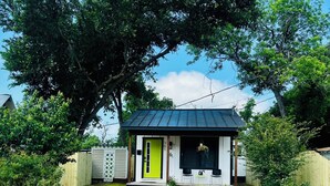 Une petite maison avec une porte verte, un toit noir et un chemin de briques menant à l’entrée.