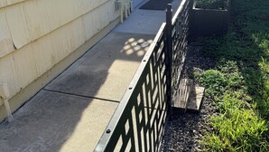 Un jardin arrière d’une maison, avec un chemin en béton, une clôture en bois et un parterre fleuri.