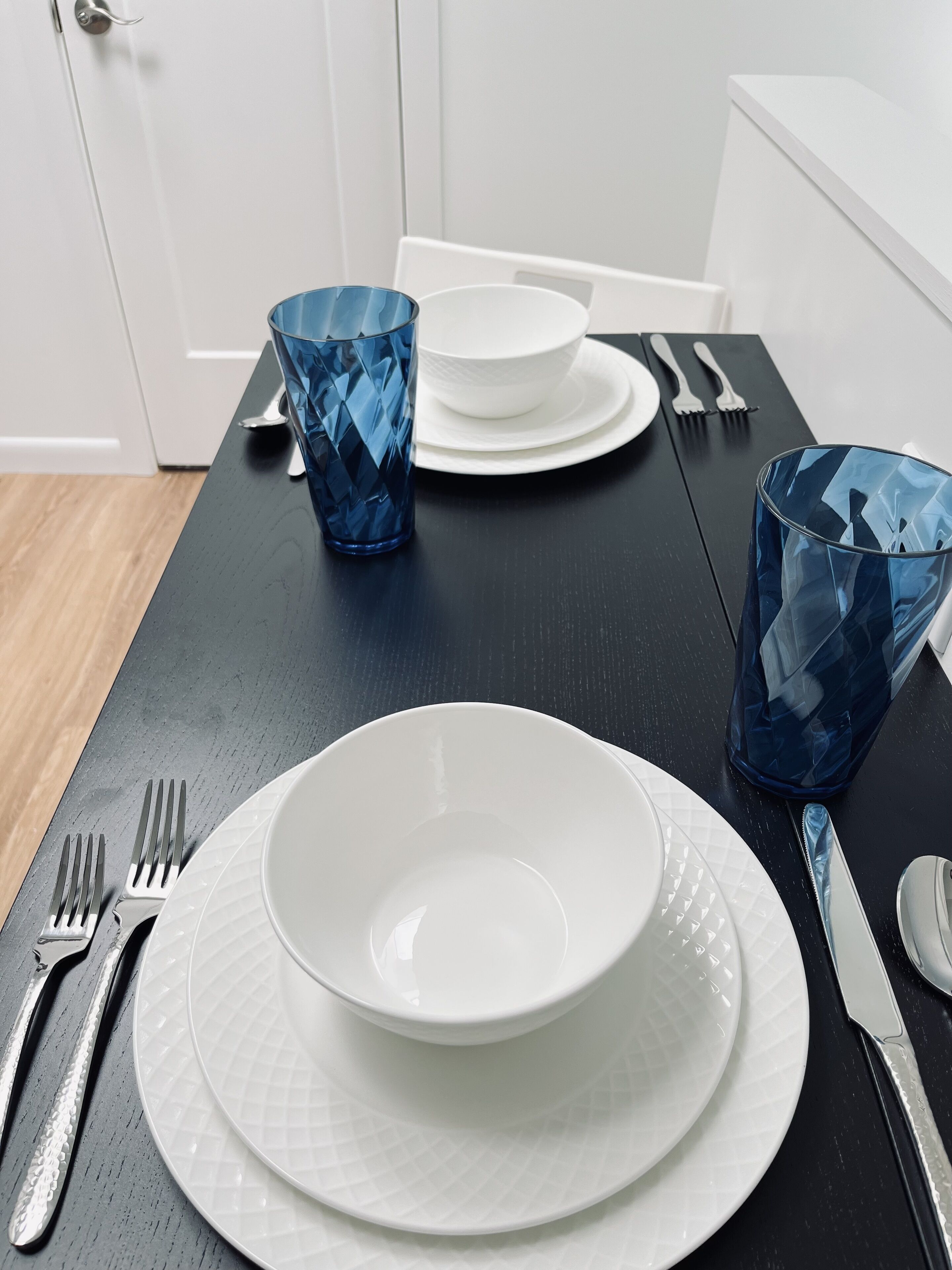 A dining table set with white plates, blue glassware, and silver cutlery.