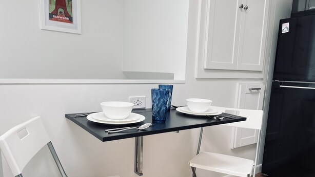 Un petit coin repas avec une table, deux chaises blanches, un vase bleu et un bol blanc.