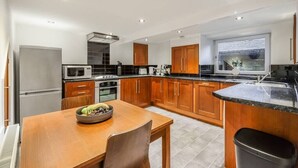 A modern kitchen with wooden cabinets, a built-in oven, a microwave, and a sink. - Sleek 2B/1B Retreat in Lindley, Huddersfield (Lindley)