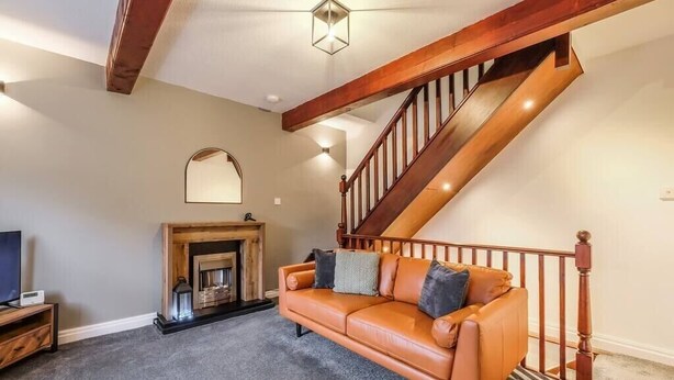 A living room with a wooden staircase, a fireplace, and a leather sofa. - Sleek 2B/1B Retreat in Lindley, Huddersfield (Lindley)