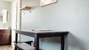 Um quarto com uma mesa de madeira escura, uma pequena prateleira e uma placa emoldurada na parede.