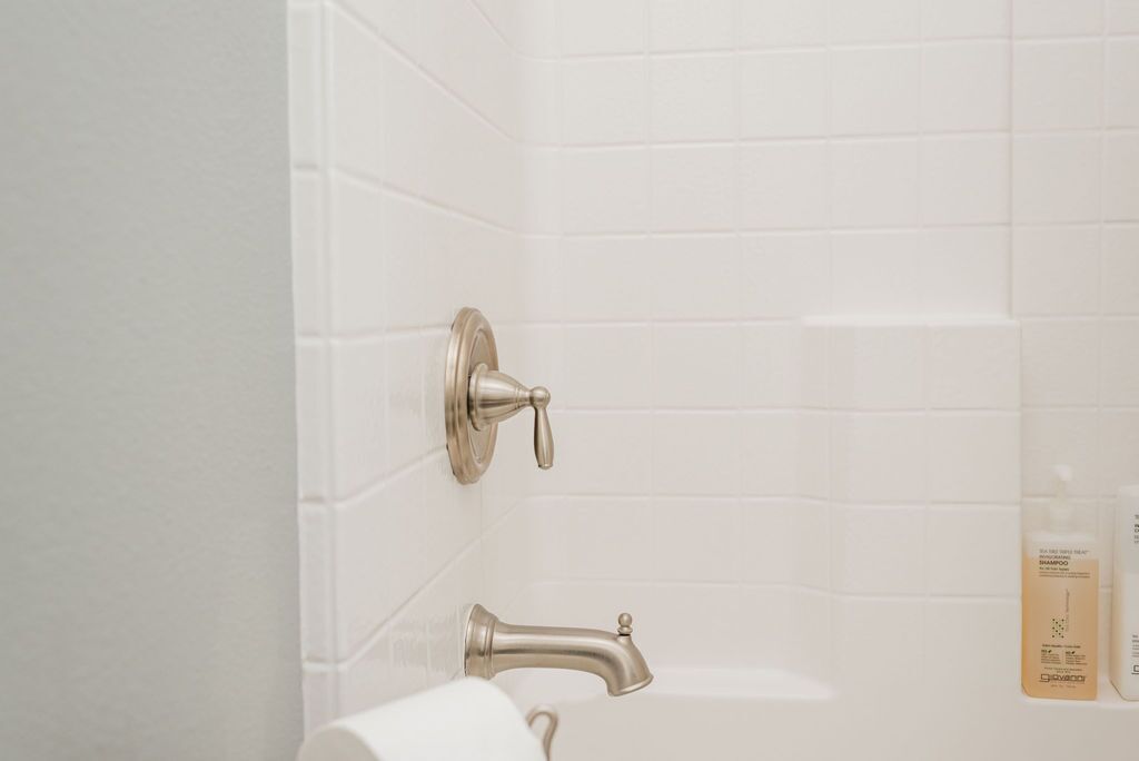 A bathroom with white tiled walls, a silver faucet, and a toilet paper holder.
