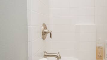 A bathroom with white tiled walls, a silver faucet, and a toilet paper holder.
