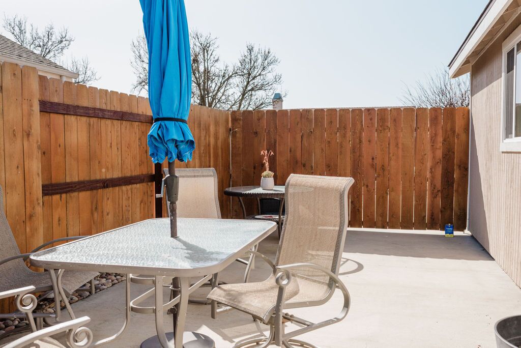 Une terrasse avec une table et des chaises en métal, un parasol bleu et une clôture en bois.