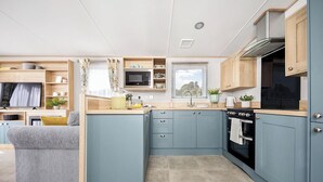 A compact kitchen with a microwave, stove, and sink, adjacent to a living area with a sofa and TV. - Platinum 3 Pet Friendly (Clunderwen, Nr Narberth)