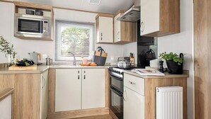 A compact kitchen with wooden cabinets, a microwave, a stove, and a sink. - Platinum 3 Pet Friendly (Clunderwen, Nr Narberth)