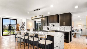 A modern kitchen with a marble island, dark cabinetry, and a large window offering a view of the outdoors. - Spacious Retreat with Heated Pool-Hot Tub-Games-Bar-Near Keeneland&Bourbon Trail (Lexington)