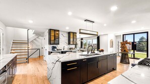 A modern kitchen with marble countertops, dark cabinetry, and a central island. - Spacious Retreat with Heated Pool-Hot Tub-Games-Bar-Near Keeneland&Bourbon Trail (Lexington)