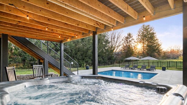 A hot tub with a wooden deck overhead, a pool, and outdoor furniture. - Spacious Retreat with Heated Pool-Hot Tub-Games-Bar-Near Keeneland&Bourbon Trail (Lexington)
