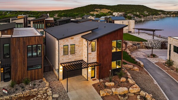 A modern house with a stone facade, a black roof, and a view of a lake.