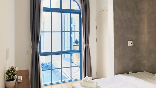 A hotel room with a large window, a bed, a bedside table with a plant, and a view of an outdoor area. - Serena Villa, Da Nang city, Vietnam, 3 bedrooms, near the beach (Đà Nẵng)
