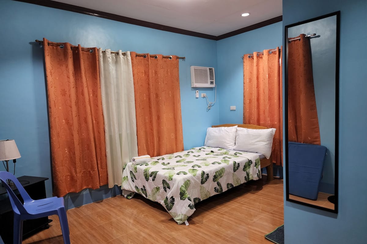 Ein Schlafzimmer mit Bett, Vorhängen, Schreibtisch und Stuhl sowie einer Klimaanlage.