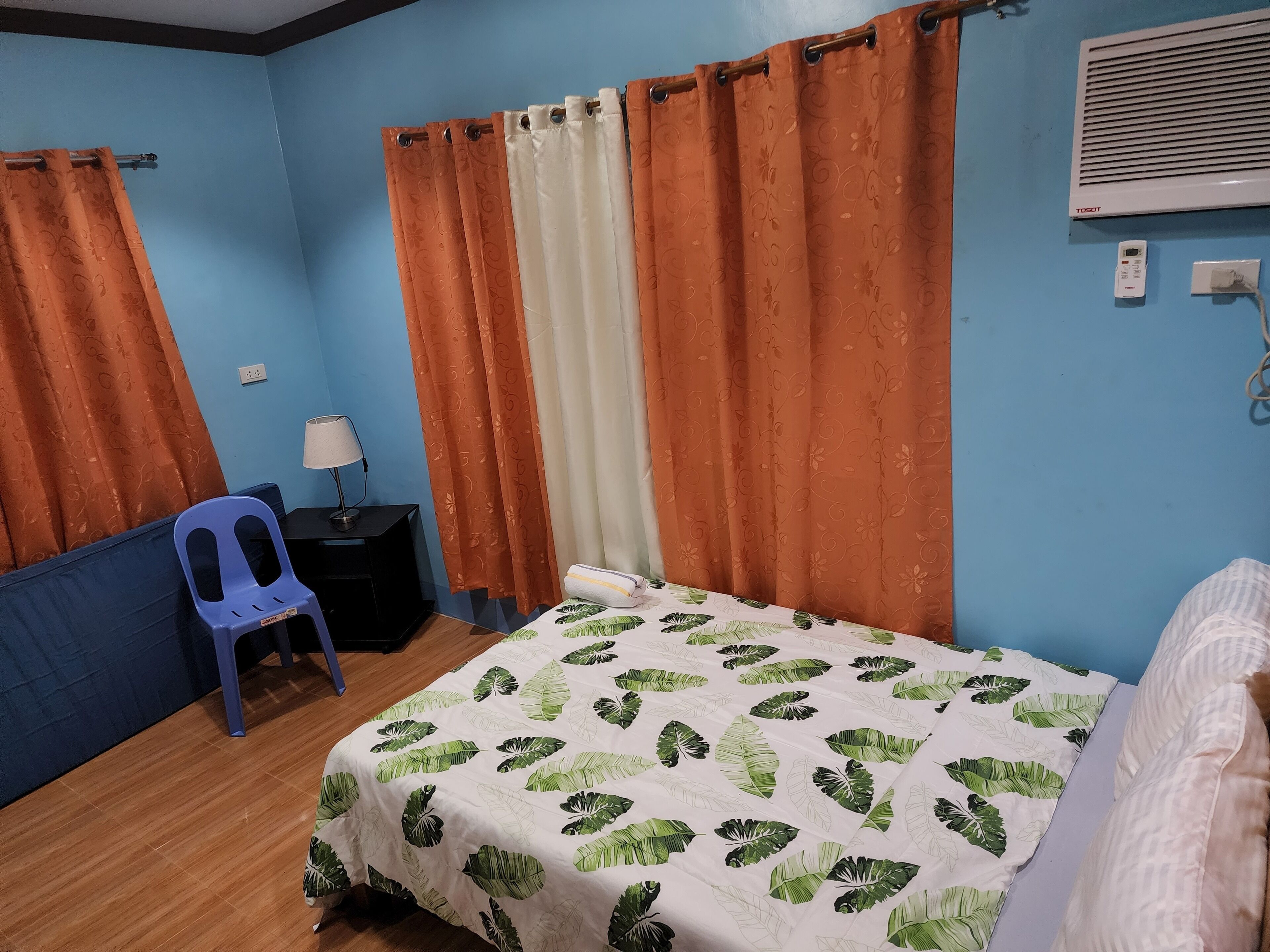 A room with a bed, a desk with a lamp, a chair, and a window with curtains.