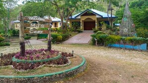 A camp entrance with a wooden sign, a building with a blue roof, and a decorative tree structure. - MJS Campsite and Mountain Resort (Balilihan)
