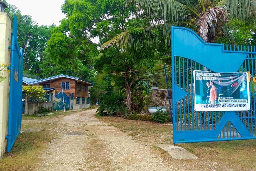 A gated entrance to a property with a blue gate, a signboard, and a building in the background.