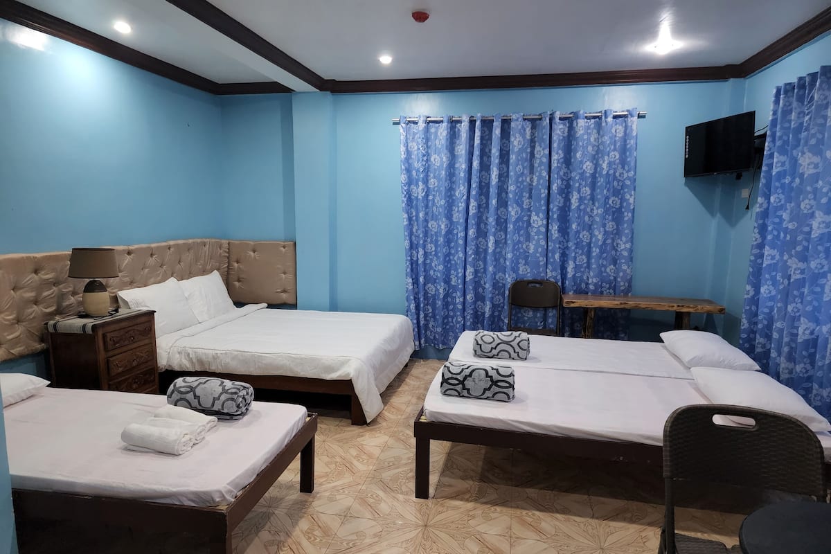 Ein Hotelzimmer mit zwei Einzelbetten, einer Holzbank, einem kleinen Tisch, einem Fernseher und einem Sessel.