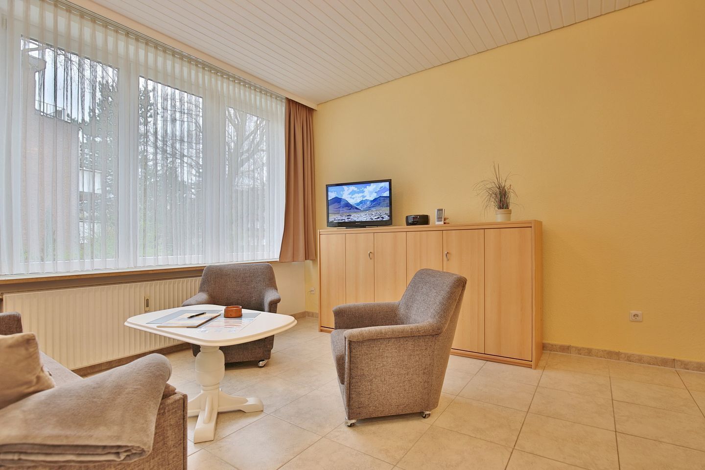 A room with a large window, a television on a cabinet, and two armchairs.