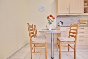 Uma cozinha pequena com uma mesa redonda, duas cadeiras de madeira, um relógio e um vaso com flores.