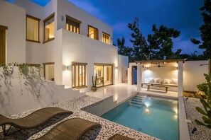 Ein modernes Haus mit Schwimmbad, Sitzgelegenheiten im Freien und einer gut beleuchteten Terrasse.