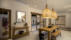 A modern dining area with a wooden table, bench, and hanging rattan light fixtures. - Villa Oasi 1 by Alfred in Bali (Pecatu)