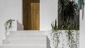 A staircase leading to a wooden door, with white walls and a small garden area with plants and pebbles. - Villa Oasi 1 by Alfred in Bali (Pecatu)