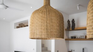 A modern kitchen with a wooden table, hanging wicker pendant lights, and built-in shelves with decorative items. - Villa Oasi 1 by Alfred in Bali (Pecatu)