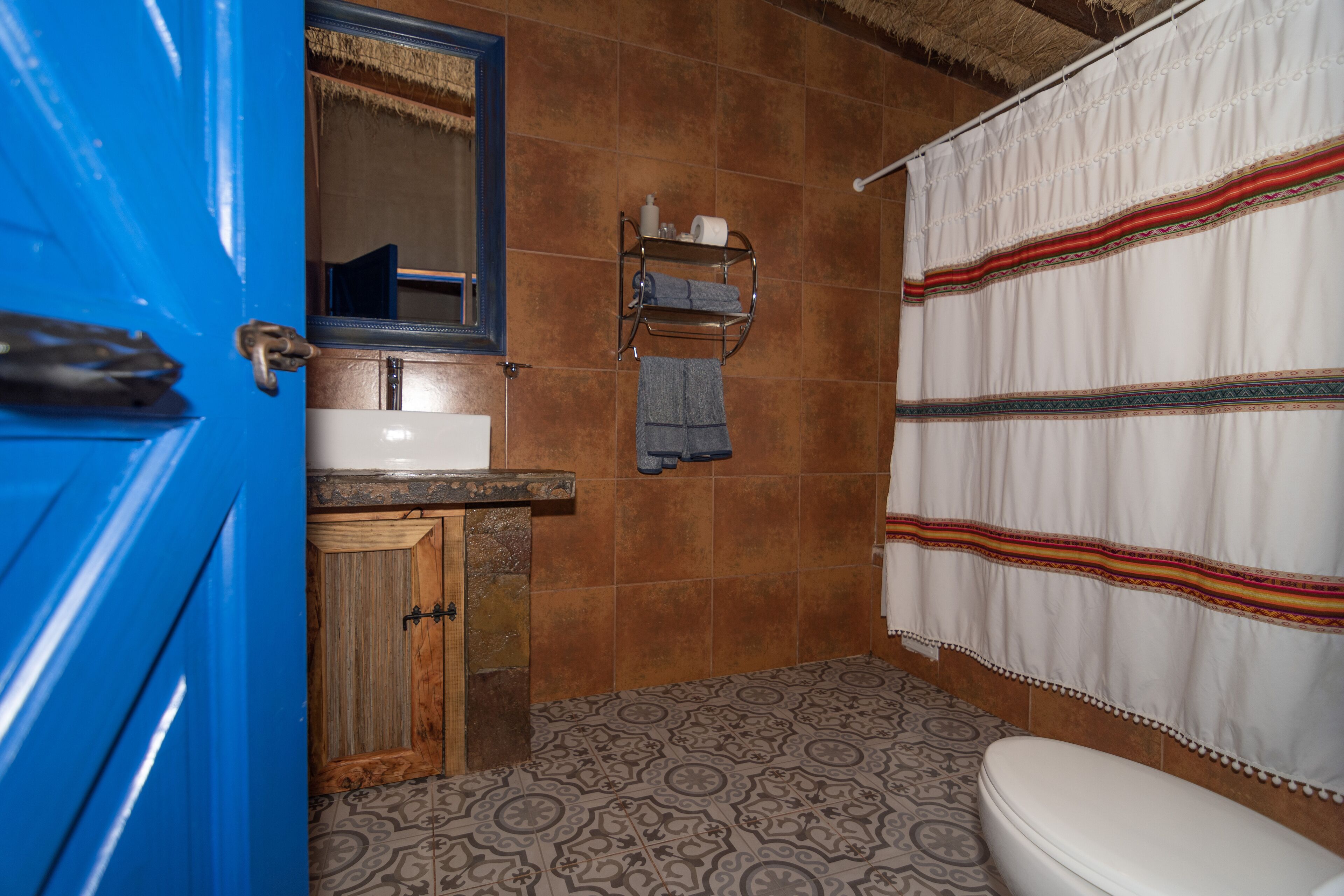 A bathroom with a blue door, a wooden cabinet, a sink, a mirror, a towel rack, a patterned floor, and a toilet.