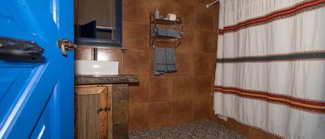 A bathroom with a blue door, a wooden cabinet, a sink, a mirror, a towel rack, a patterned floor, and a toilet.