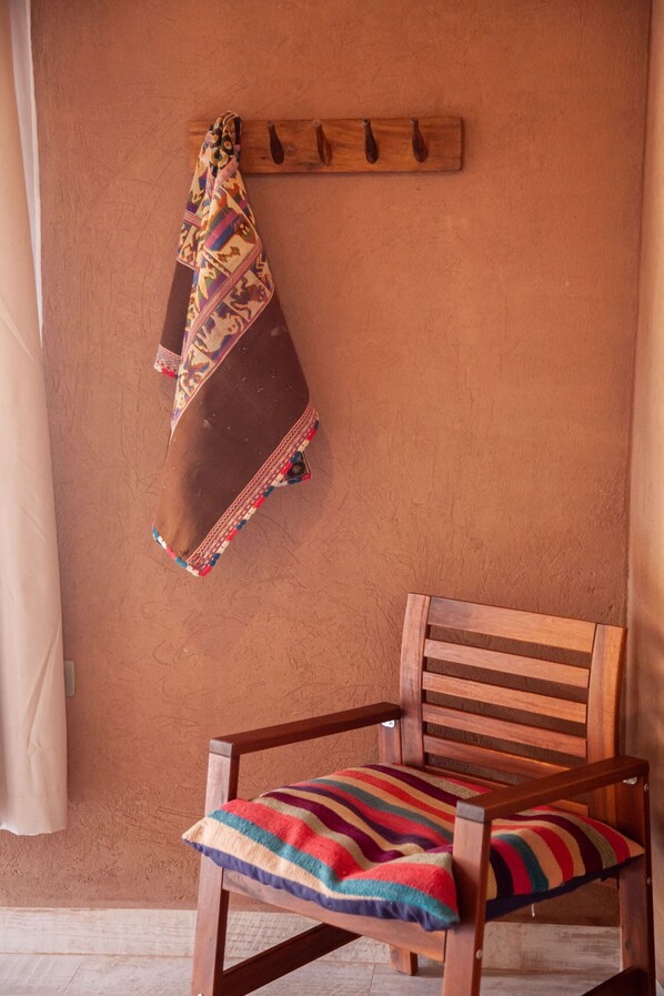 A wooden chair with a colorful striped cushion, a wooden coat rack with a patterned cloth, and a plain wall. - Ckoi Atacama Lodge (San Pedro de Atacama)