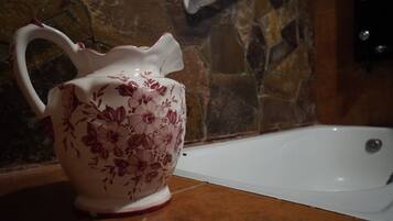 A white ceramic pitcher with floral designs on a countertop next to a bathtub.