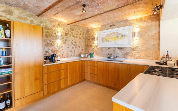 A kitchen with wooden cabinets, a stone wall, and a fish painting.