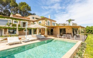 A poolside area with lounge chairs, a pergola, and a stone building with a garden.