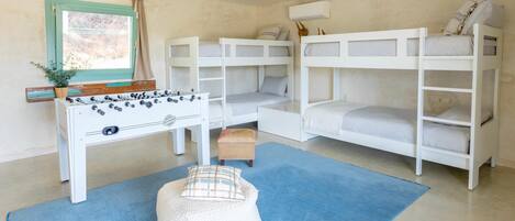 A room with bunk beds, a foosball table, a window with curtains, and a ceiling fan.