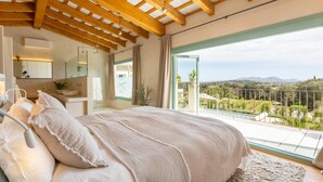 Un dormitori amb un llit gran, un bany amb un lavabo i un mirall, i un balcó amb vistes al camp.
