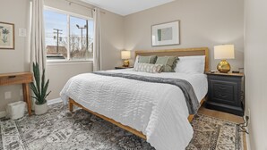 A bedroom with a bed, bedside tables, a window, a potted plant, and a rug. - NEW! Cozy 1BR Flat w/ King Bed & Workspace (Roseville)