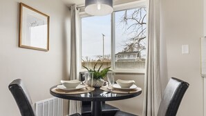 A dining area with a round table set for four, a vase with greenery, and a window with a view of buildings and trees. - NEW! Cozy 1BR Flat w/ King Bed & Workspace (Roseville)