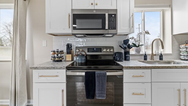 A modern kitchen with white cabinets, a built-in microwave, a stove, and a sink. - NEW! Cozy 1BR Flat w/ King Bed & Workspace (Roseville)