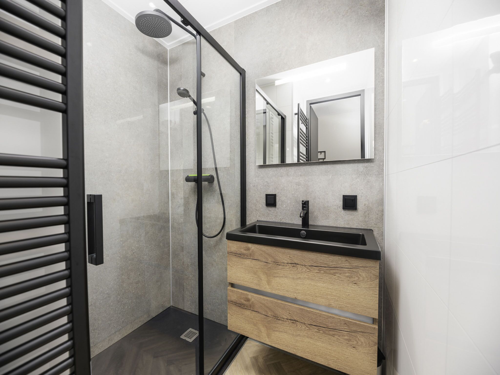 Ein modernes Badezimmer mit einer gläsernen Duschkabine, einem Holzwaschtisch mit schwarzem Becken und einem großen Spiegel darüber.