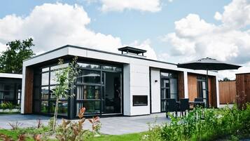 A modern two-story building with large glass windows, a patio area with outdoor seating, and a wooden fence in the background.