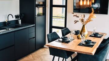Een moderne keuken met zwarte kastjes, een houten eettafel gedekt voor vier personen en een groot raam dat voor natuurlijk licht zorgt.