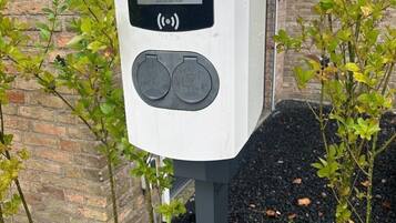 A public charging station branded '50five e-mobility' with two charging ports, located outdoors near a brick building and surrounded by greenery.