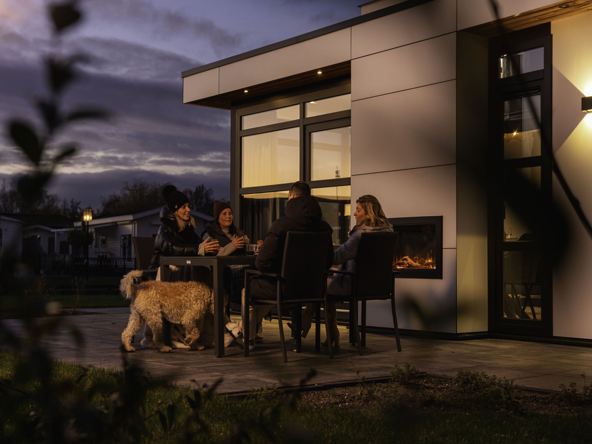 A modern outdoor seating area with a fireplace, surrounded by a contemporary building with large windows.