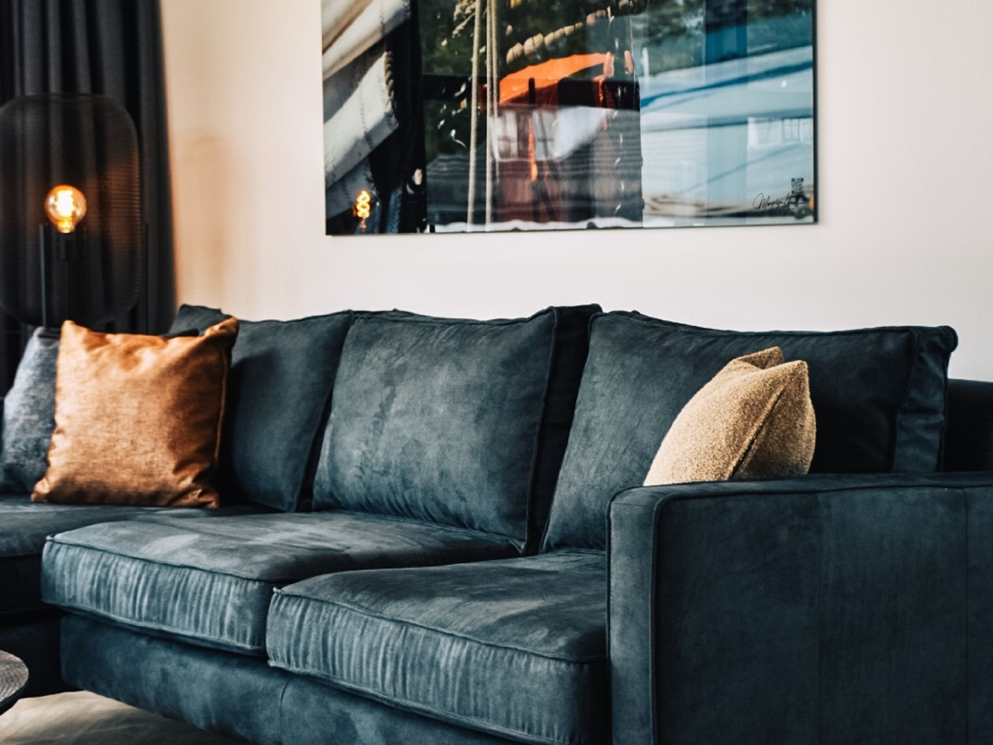 A dark grey sofa with multiple cushions, a lamp, and a framed picture on the wall.