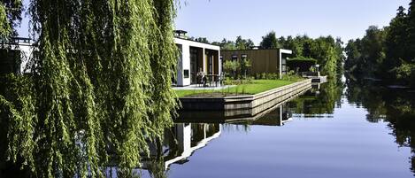 A calm river with a modern building and a weeping willow tree on the left.
